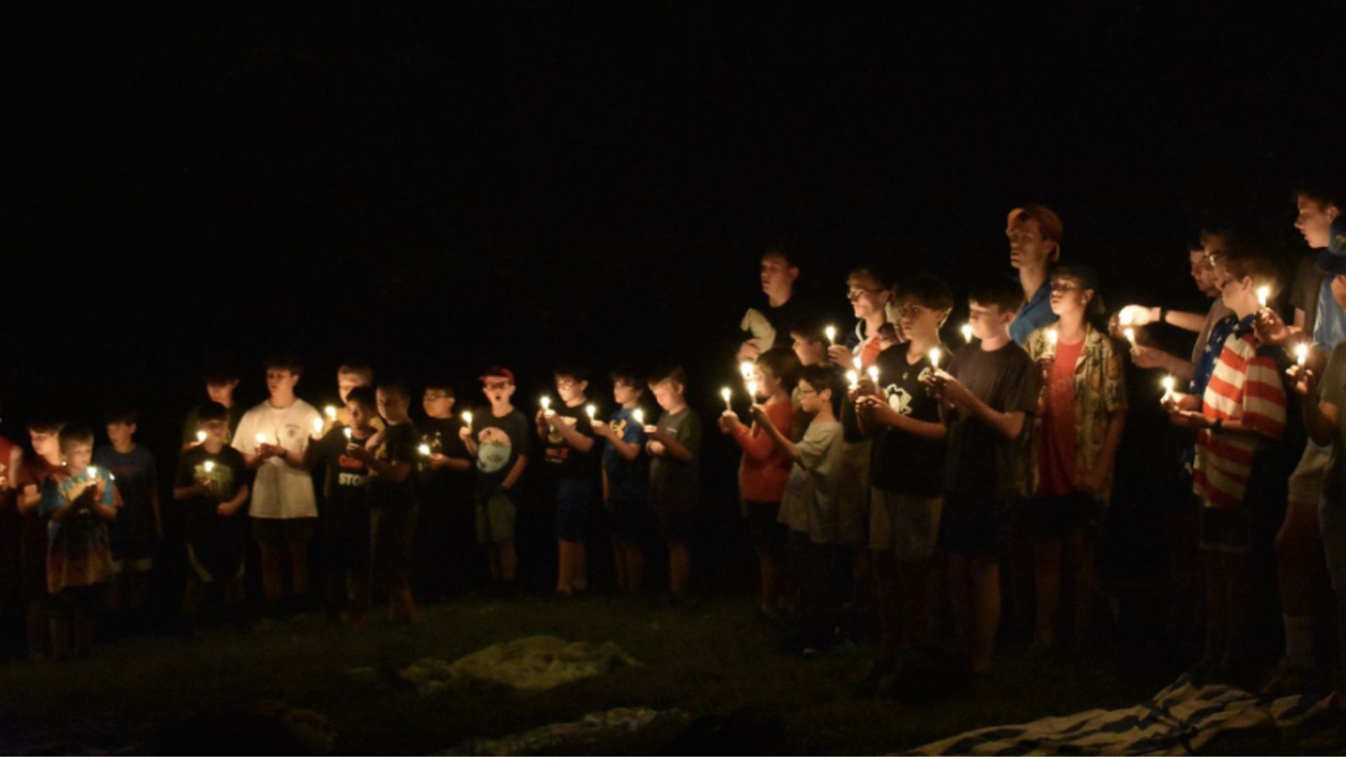 A group of children and adults stand in darkness holding glowing candles.